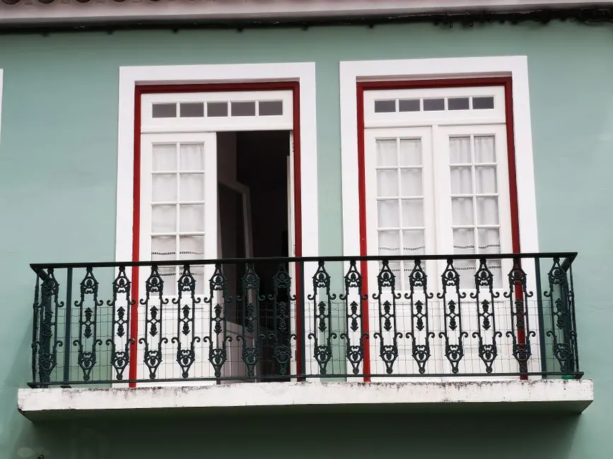 A beautifully designed balcony with ornate ironwork and white French doors on a green facade.